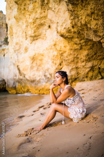 Thinking latin girl sitting on sand at beach and looking at ocean feel alone. Summer vocation