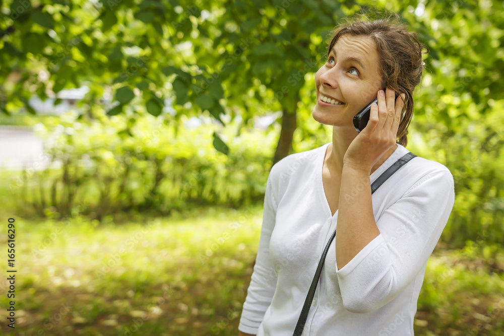 Beautiful young girl is calling by phone in green summer park Beautiful young girl is calling by phone in green summer park