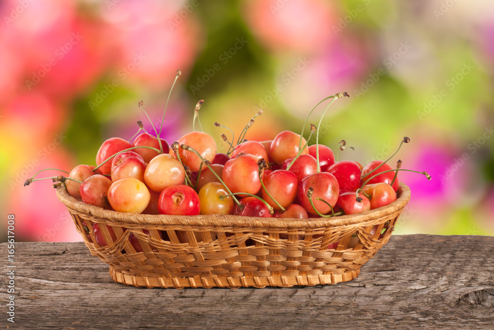 Yellow cherry in a wicker basket on a wooden table with a blurry garden background Yellow cherry in a wicker basket on a wooden table with a blurry garden background