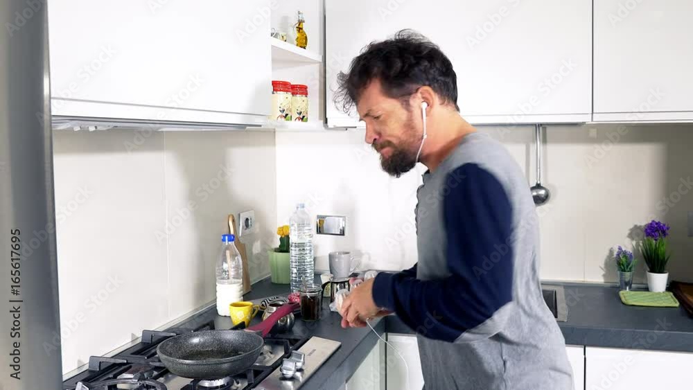 Happy man cooking eggs in kitchen while dancing and listening music Happy man cooking eggs in kitchen while dancing and listening music