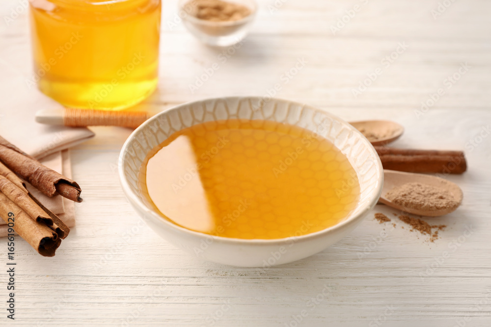 Bowl with honey and cinnamon on light table