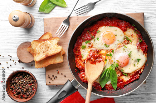 Fototapeta Frying pan with eggs in purgatory on wooden background
