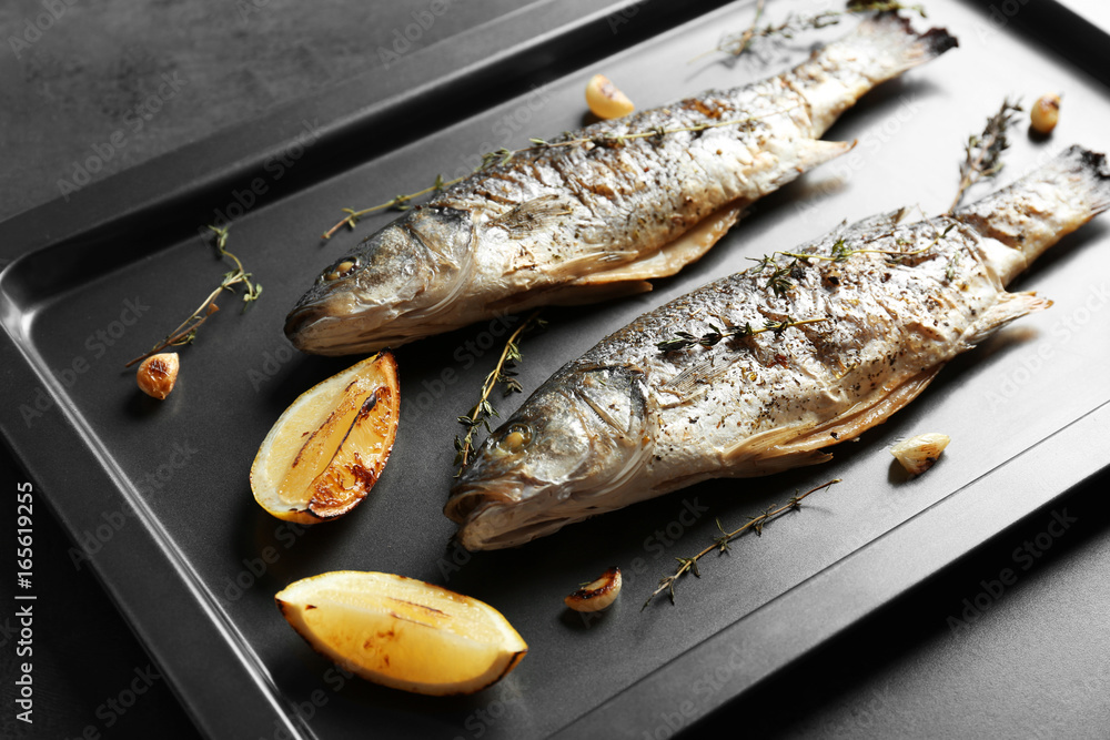 Baking sheet with fried fish on dark background
