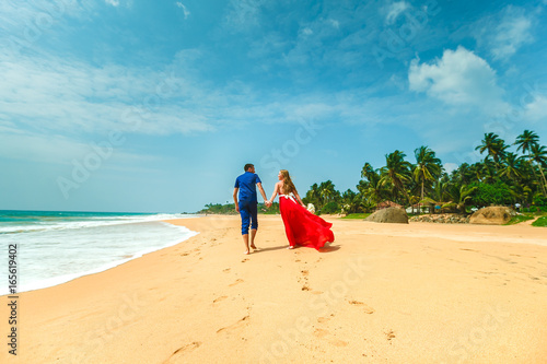 Honeymoon at the sea. Back view of loving couple walking away with footprints at sandy beach. Holding hands