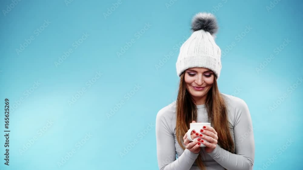Woman in winter cap gray sports thermal underwear for skiing training holds mug with tea or coffee warming herself. Winter sport activity. Beautiful long hair sportswoman on blue studio shot, full HD. Woman in winter cap gray sports thermal underwear for skiing training holds mug with tea or coffee warming herself. Winter sport activity. Beautiful long hair sportswoman on blue studio shot, full HD.