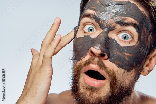 A man with a beard on a white isolated background apply clay cosmetic face mask