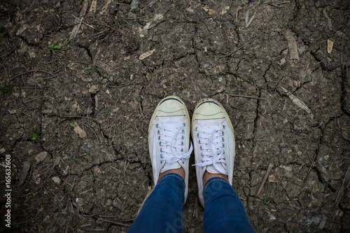 white sneakers stand on dry soil.