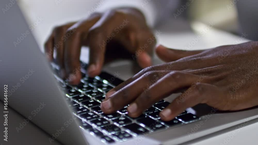 Closeup of hands of African man typing on laptop keyboard with illuminated letters