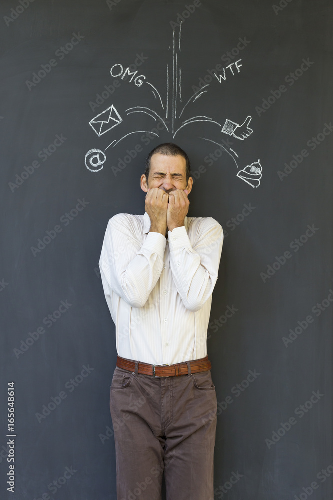 Single white adult man standing in front of a blackboard with drawn social media icons symbolizing frustration, stress and overload from modern communication Single white adult man standing in front of a blackboard with drawn social media icons symbolizing frustration, stress and overload from modern communication
