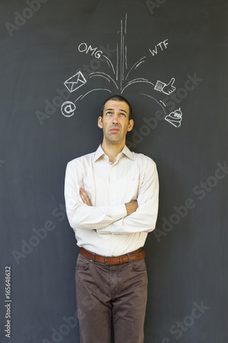 Single white adult man standing in front of a blackboard with drawn social media icons symbolizing frustration  stress and overload from modern communication