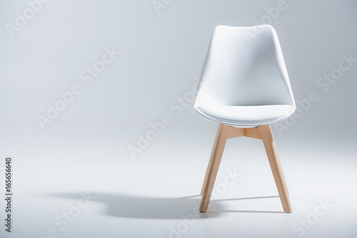 Studio shot of stylish chair with white top and light wooden legs standing on white photo