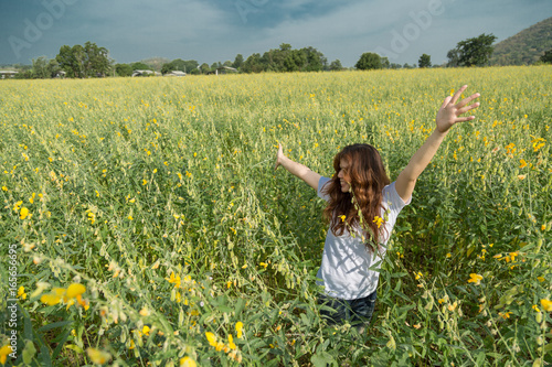 asian women with slightly curly is raising arms to the sky in yellow field at summer, Thailand.