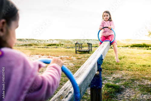 Φωτογραφία Little twin girls children are riding seesaw swing in park.