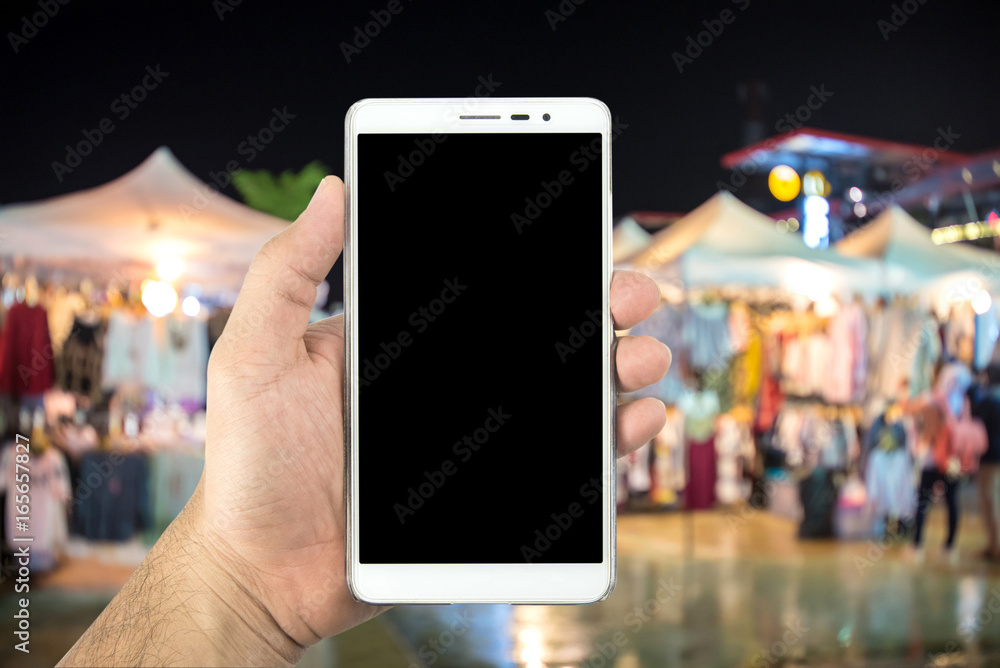 Man's hand holding smartphone and blurred image of street market at night. Man's hand holding smartphone and blurred image of street market at night.