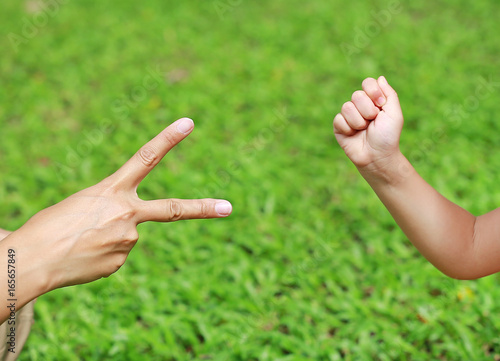 Hands of mother and daughter, Scissors and rock - hands on green grass background. © zilvergolf