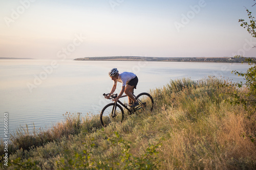 Bicycle rider on professional cyclocross bike ride downhill, pine and lake background 