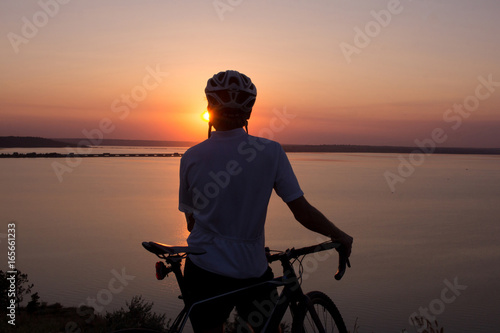 silhouette of a cyclist watching sunset in lake, male bicycle rider in helmet during sunset 