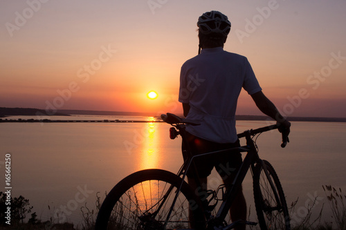 silhouette of a cyclist  watching sunset in lake  male bicycle rider in helmet during sunset 