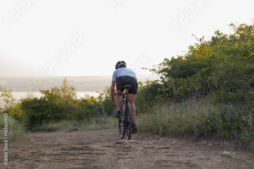 Bicycle racer ride alone on the rocky road, lake and forest background 