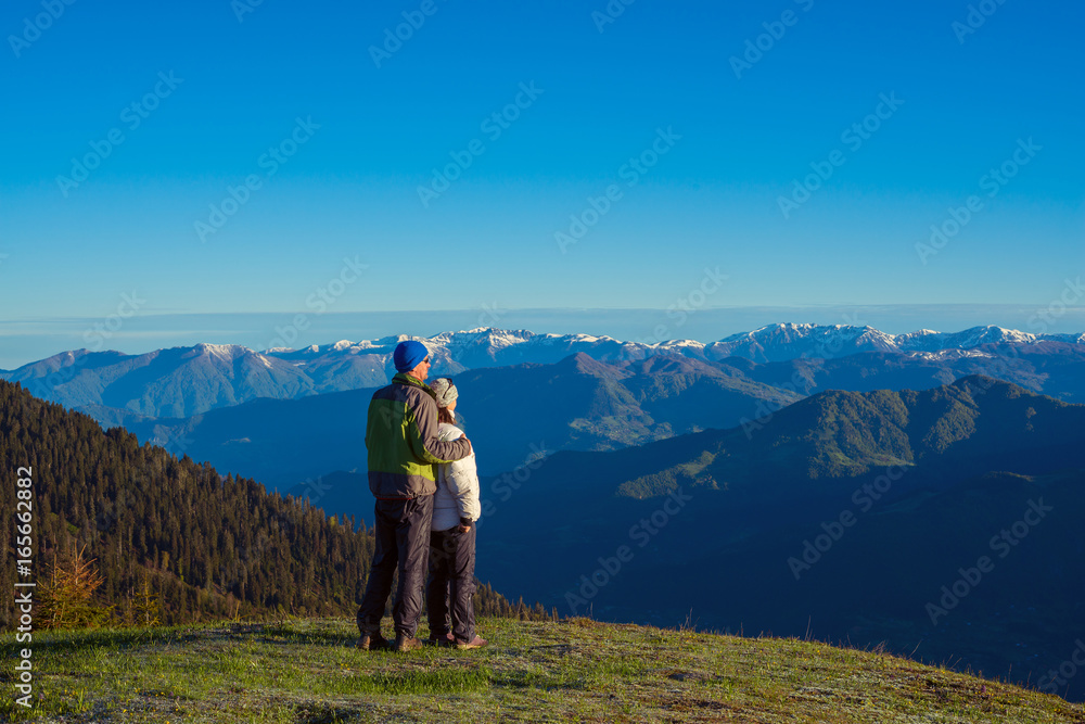 Couple of travelers, hugging, is admiring the dawn in the mountains