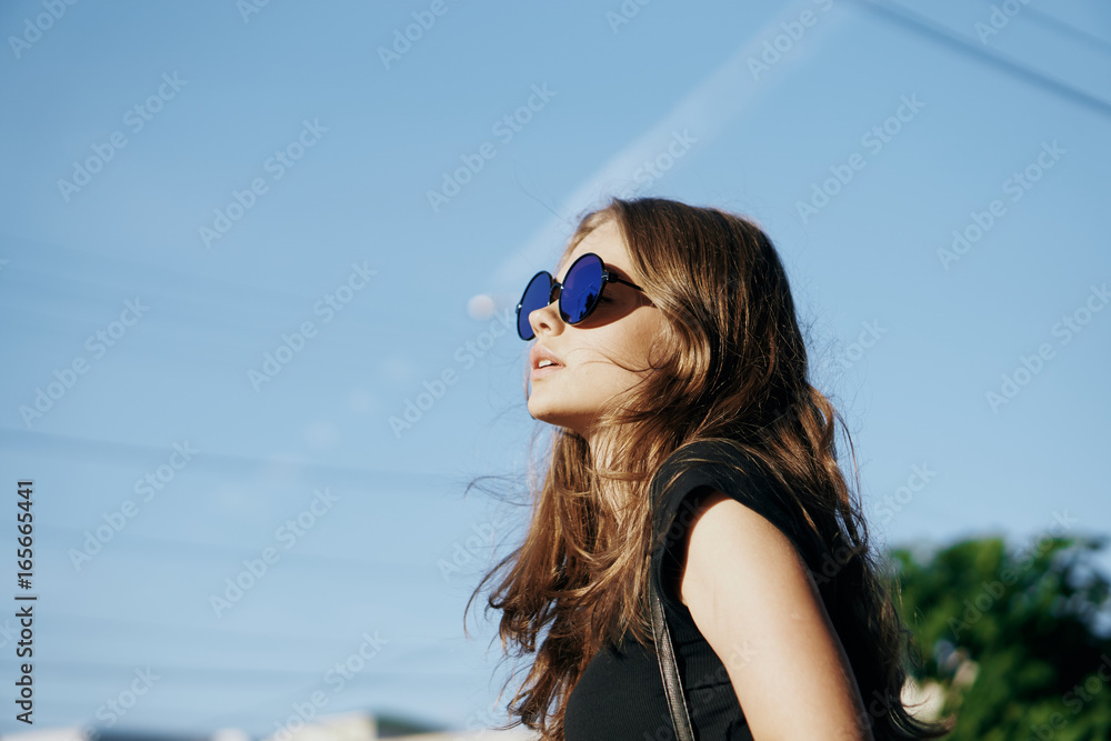 Young beautiful woman in sunglasses walking along a street in a city in the fresh air