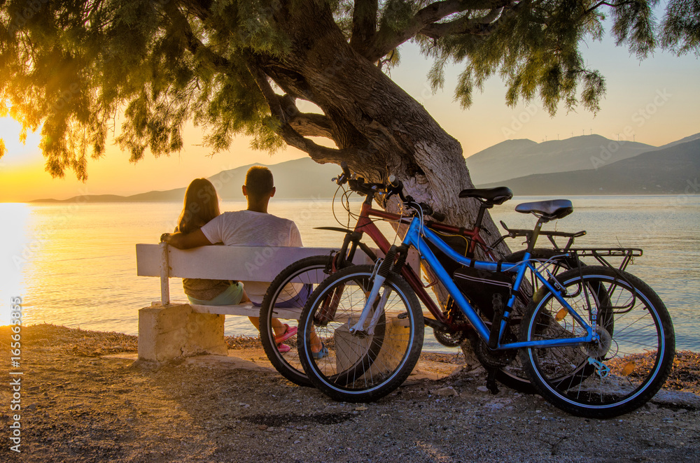 Fototapeta premium A couple of lovers watching the sunset sitting on a bench by the sea.