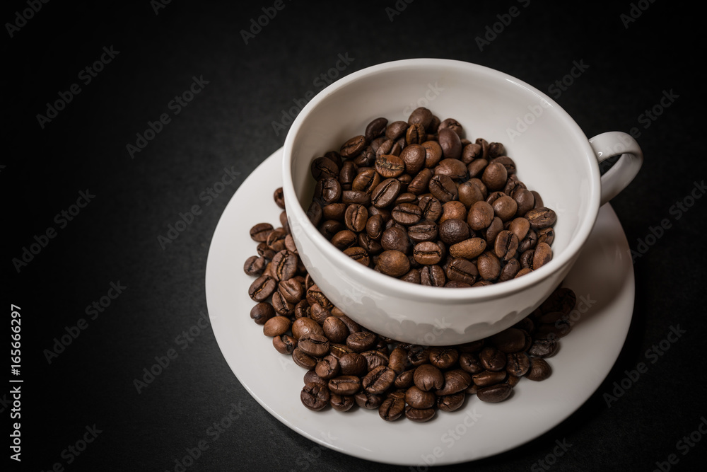 Roasted coffee beans in white cup on dark background. Selective focus.