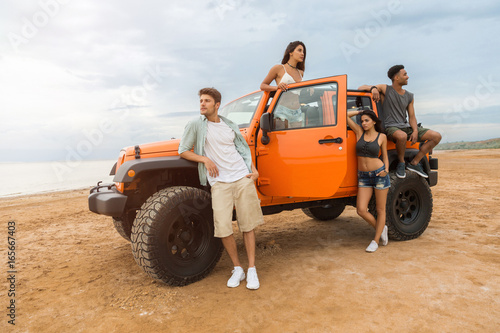 Group of young cheerful people standing near their car