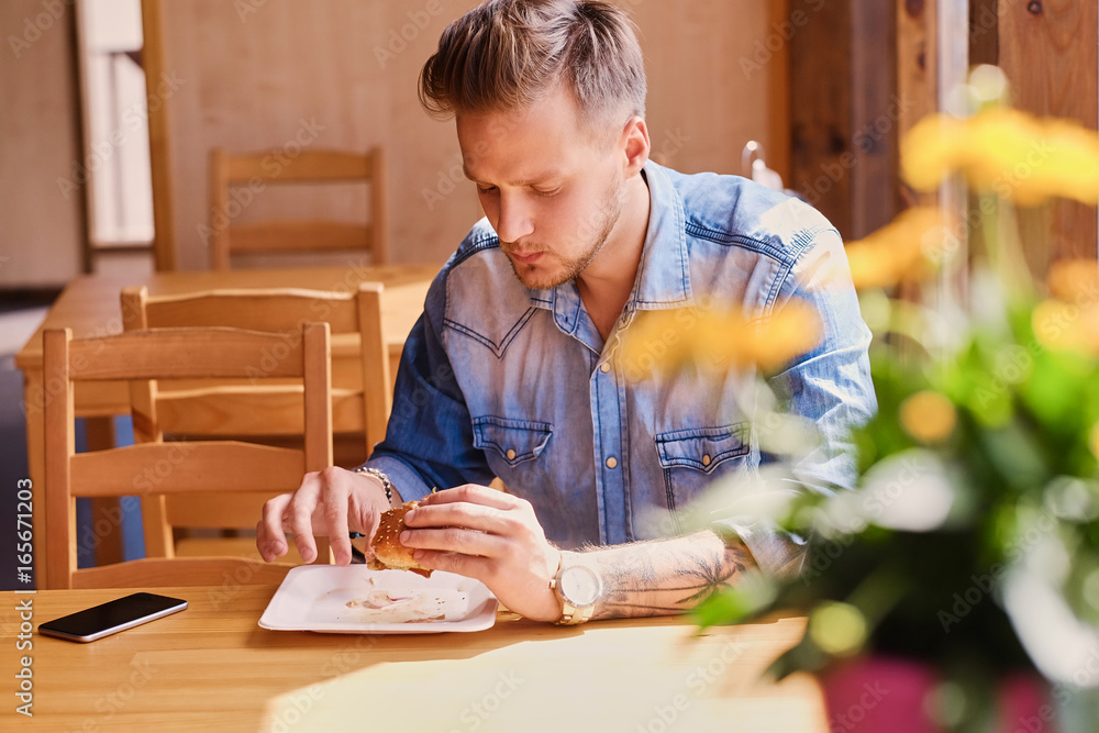 A man in denim jacket eats vegan burger. A man in denim jacket eats vegan burger.