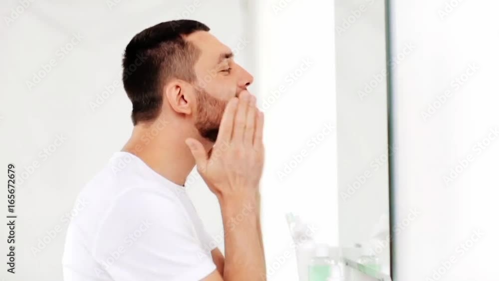happy man applying aftershave to face at bathroom happy man applying aftershave to face at bathroom