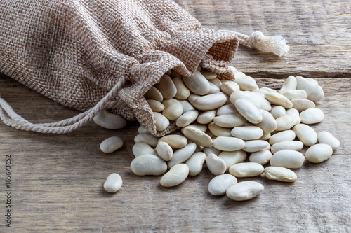 Dried white beans in a bag on a wooden background