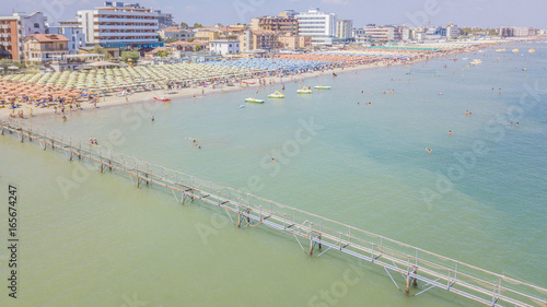 Dalla riviera romagnola vista aerea di ombrelloni colorati disposti in fila sulla spiaggia di Riccione. le persone in spiaggia prendono il sole o si riparano all' ombra prima di un bagno a mare. photo