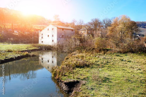 Autumn landscape of the countryside: old non-working watermill near greenfields and flowing river
