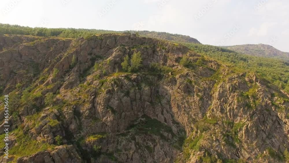 AERIAL: A huge cliff covered with trees during sunset. Mountain range in perspective, lovely landscape, soft lighted rocks, blurred horizon, wild nature. AERIAL: A huge cliff covered with trees during sunset. Mountain range in perspective, lovely landscape, soft lighted rocks, blurred horizon, wild nature.