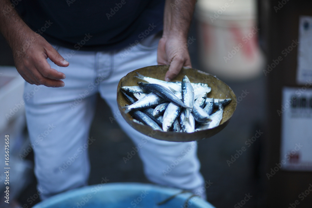 A merchant in the fish market holds fish in a pan of weights
