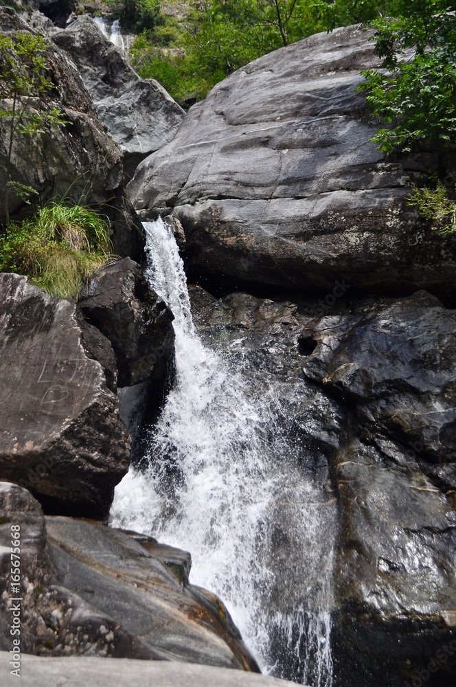 Obraz premium Wasserfall von Bergbach sprudelt zwischen Felsen und Gestein aus dem Berg ins Maggia Tal. Tessin, Schweiz