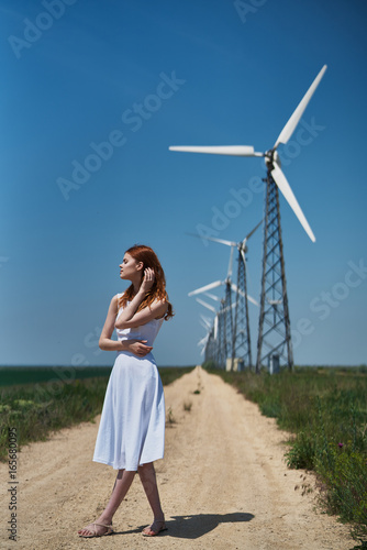 Young beautiful woman in a white dress in a field on a background of windmills, summer