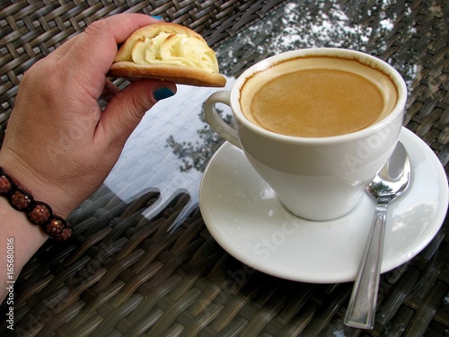 Hand bracelet holds sochnik and next to a table in a cafe is a Cup of Americano. photo