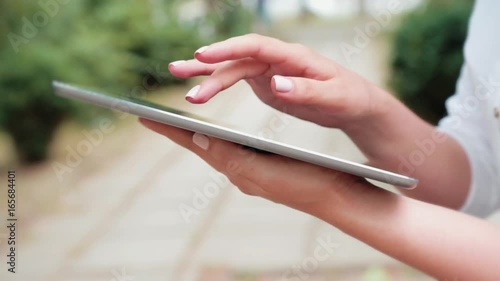 Closeup of female hands using modern digital tablet outdoor, technology and social networking concept, woman typing on a touch screen of portable computer, bokeh light blurred background