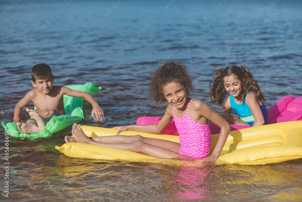 Obraz premium multiethnic little children swimming on colorful inflatable mattresses at sea together