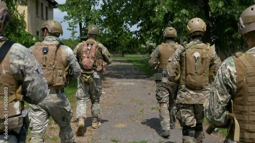 Group of soldiers carrying their weapon patrolling among the trees and ruined buildings