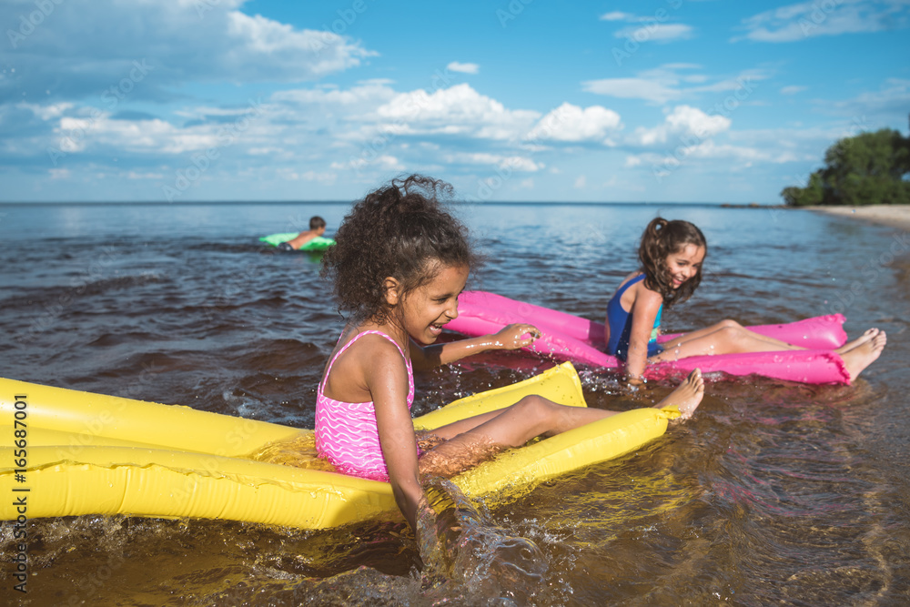 Obraz premium multicultural happy girls swimming together on inflatable mattresses at sea