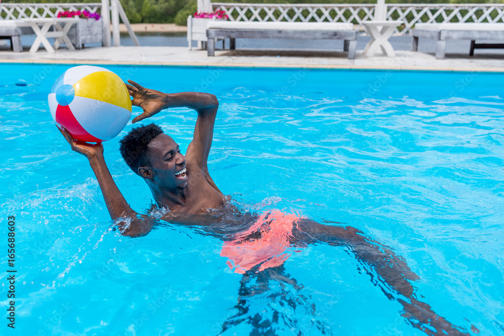 Young happy african american man playing with ball in swimming pool