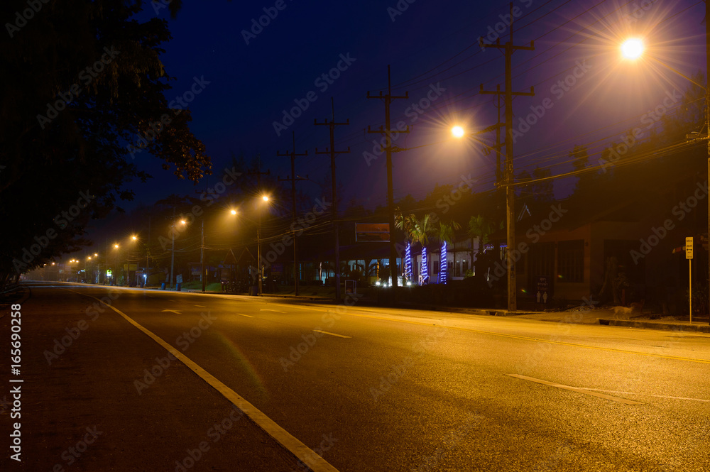 Empty street at early morning before dawn shrouded in mist illuminated by streets lights