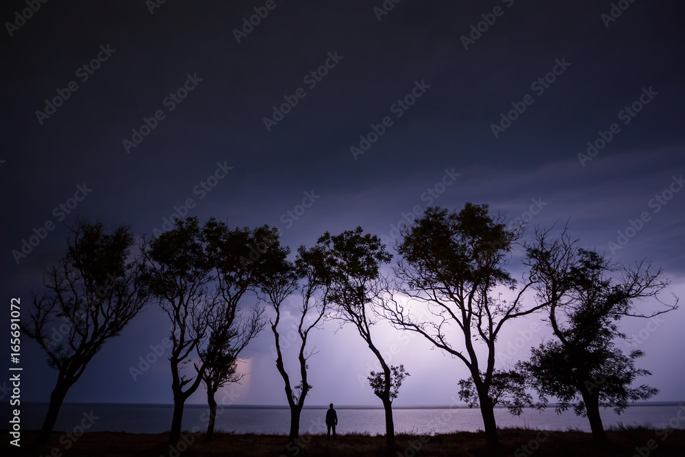  a man is standing by the sea during a thunderstorm