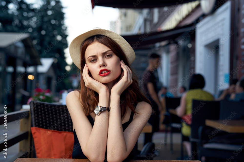 Young beautiful woman in a hat sits in a cafe on a street in a city on a terrace