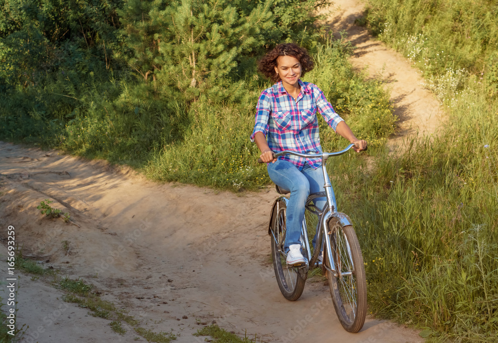 Naklejka premium Young woman rides a bicycle in the park on sunset background