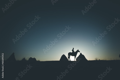 Man and horse silhouette on the background of valley at Cappadocia Anatolia Turkey.The great tourist attraction of Cappadocia best places to fly with hot air balloons.Rocks looking like mushrooms.