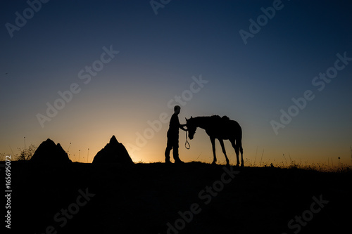 Man and horse silhouette on the background of valley at Cappadocia Anatolia Turkey.The great tourist attraction of Cappadocia best places to fly with hot air balloons.Rocks looking like mushrooms.