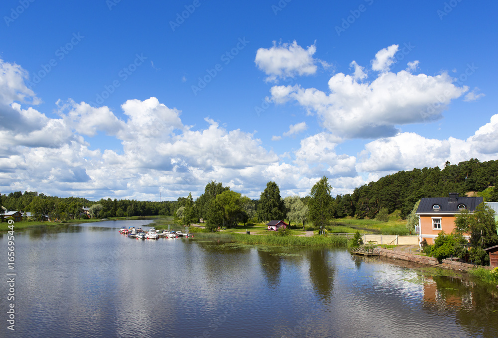 Beautiful scenery in the countryside next to a river in Finland. Sunny summer day with some clouds in the sky. Traditional village view.